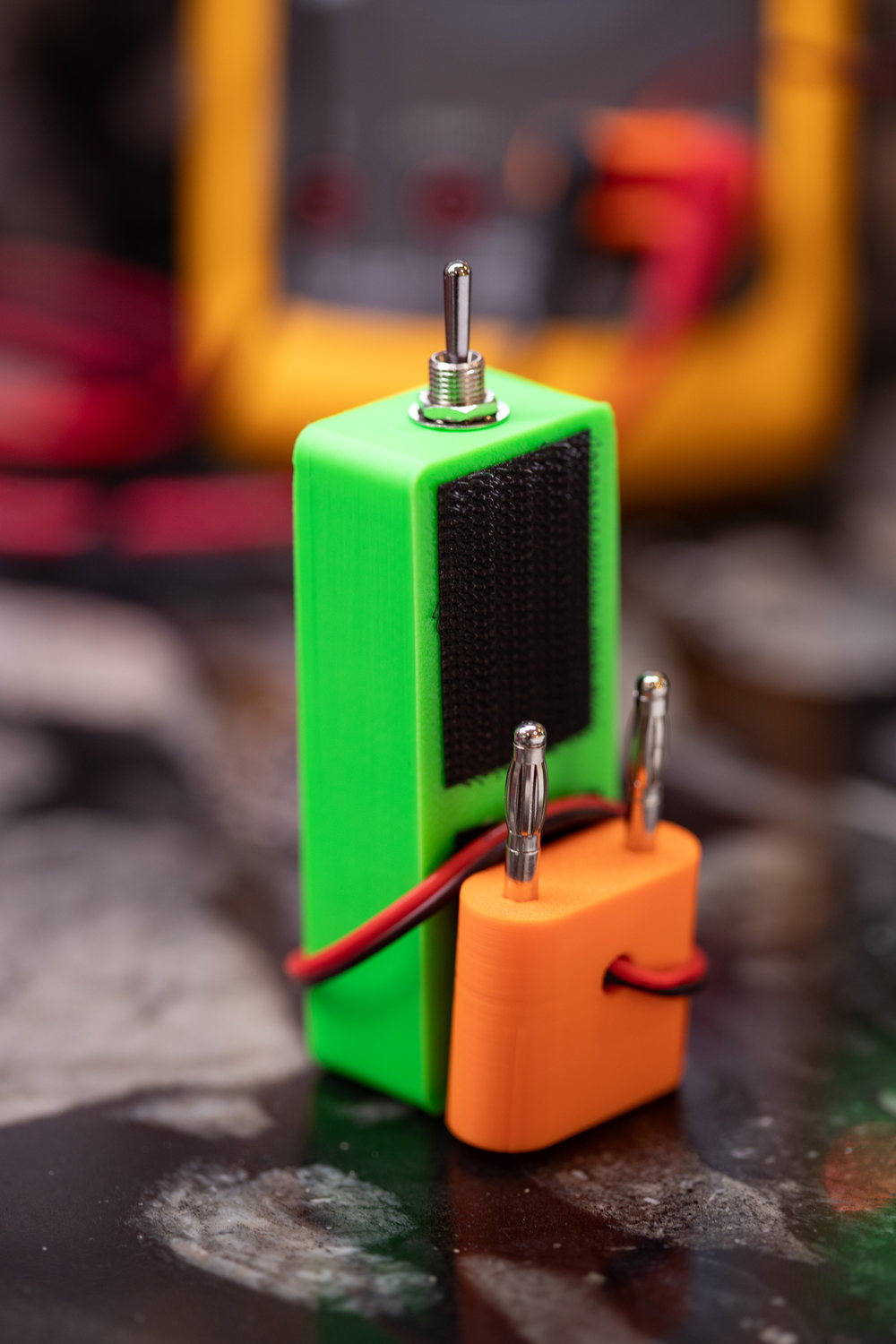 The back of a Blinky Hawk, showing the black hook-and-loop pad that sticks it to a meter, and the stacking banana pins with an orange stacking plug pushed onto them.